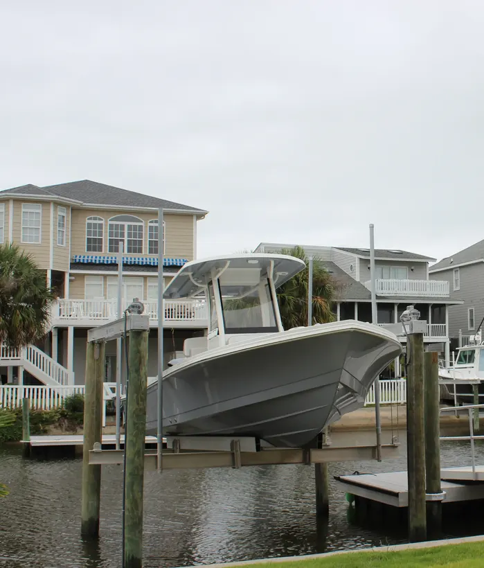 Center-console boat on a piling-supported lift, showing the cradle and dock connection