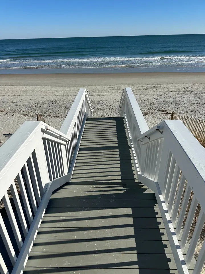 Completed beach-access stairs with white railings descending from a Charlestowne Grant dune walkover