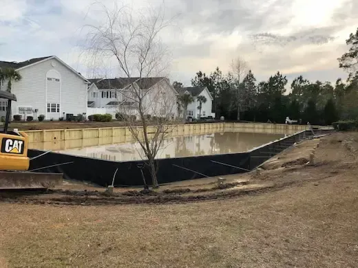 Side view of The Villas pond with the timber perimeter, surrounding homes, and a tree in the foreground