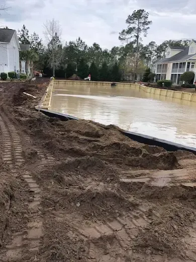 Construction-stage ground beside The Villas retention pond with timber walls along the opposite edge