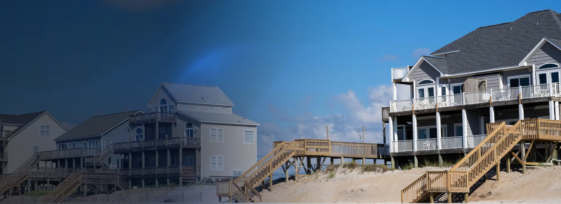Coastal homes with elevated decks, stairs, and a dune walkover leading toward the beach